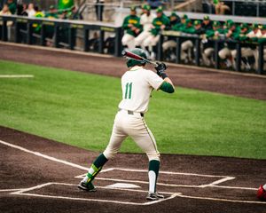 Baseball player wearing number 11 in green and white uniform stands at home plate ready to bat.