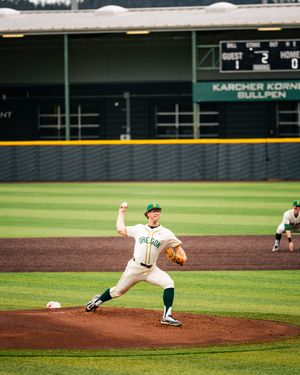 Oregon Ducks pitcher in white and green uniform delivers a pitch at PK Park baseball stadium.