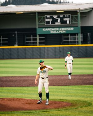 Baseball pitcher on mound at Karcher Korner Bullpen stadium, wearing green and white uniform, mid-throw during game.