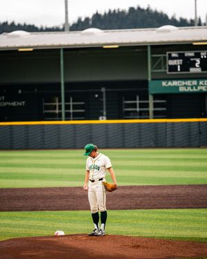 Baseball pitcher in green cap and uniform stands on mound at Karcher Ko Bullpen stadium during a game.