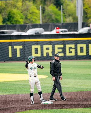 Oregon Ducks baseball player celebrates at second base during a game at PK Park, with an umpire standing nearby.