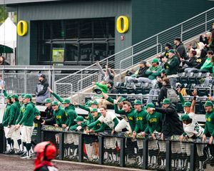 Oregon Ducks baseball team cheering in the dugout during a game at PK Park stadium.