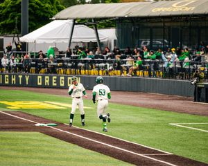 Oregon Ducks baseball players in green uniforms run the bases at Mighty Oregon field during a game.