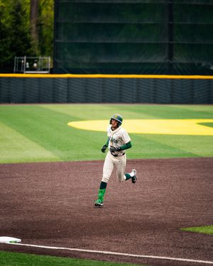 Baseball player in green and white uniform rounding the bases at a college baseball stadium.
