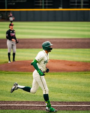 Baseball player in green Oregon Ducks uniform running bases after a hit during a college game.