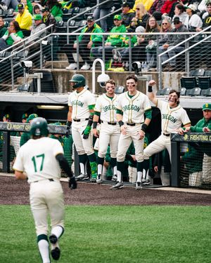 Oregon Ducks baseball players celebrate in the dugout as player number 17 jogs toward them during a game.
