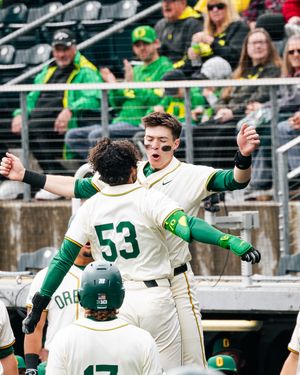 Oregon Ducks baseball players celebrate on field, player #53 embraced by teammate in green and white uniforms.
