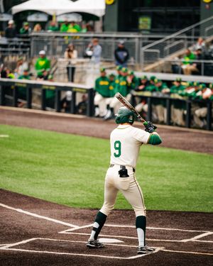Baseball player wearing number 9 in green and white uniform stands at bat during a college baseball game.