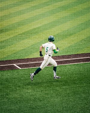 Baseball player wearing number 5 in green uniform sprinting across the field during a game.