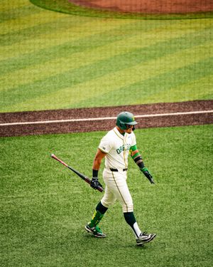 Oregon Ducks baseball player in green uniform walks with bat after at-bat in a college baseball game.