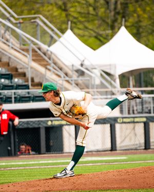 College baseball pitcher in green and white uniform mid-throw on the mound during a game.