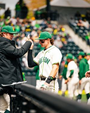 Oregon Ducks baseball player receives high five from coach during game at PK Park in green and white uniform.