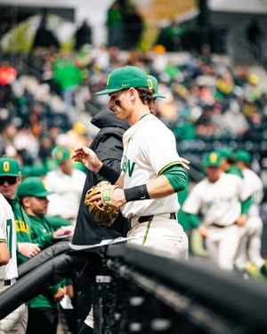 Oregon Ducks baseball player in green and white uniform holding a glove near the dugout during a game.