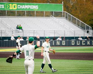 Oregon Ducks baseball players exchange a high-five on the field at a Big Ten Champions stadium during a game.