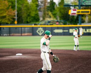 Baseball player in green and white uniform stands on field holding glove near pitchers mound during game.