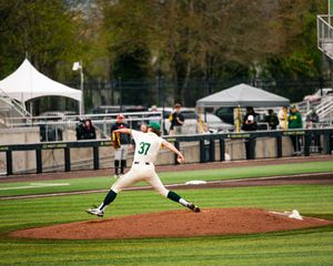 Baseball pitcher #37 in white uniform delivers a pitch on a green field during a college baseball game.
