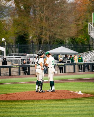 Baseball players in green and white uniforms having a mound meeting during a college baseball game on a sunny day.