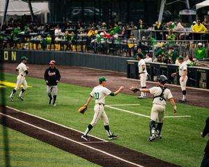 Baseball players celebrate on the field during a game at a green stadium with fans watching in the background.