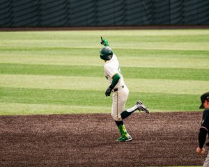 Baseball player in green uniform rounds the bases with finger pointed up after hitting a home run.