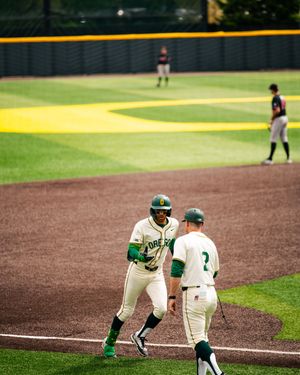 Oregon Ducks baseball player rounds third base, greeted by coach during a college baseball game at PK Park.