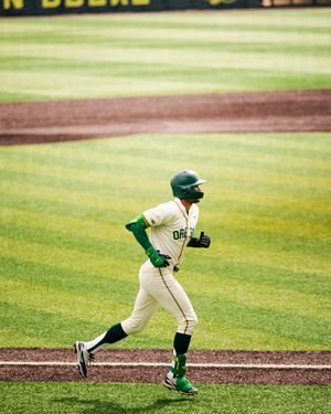 Oregon Ducks baseball player in white and green uniform running bases at a college baseball game.
