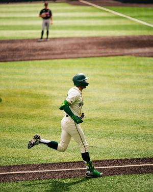 Baseball player in green uniform running bases during a college baseball game on a sunny day.