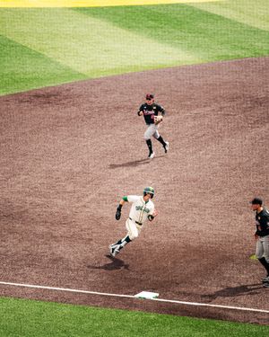 Oregon Ducks baseball player rounds third base during a college baseball game with umpire nearby.