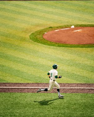 Baseball player in green and white uniform rounding the bases on a lush green field during a game.
