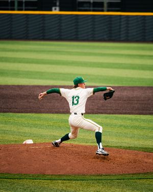 Baseball pitcher in green and white uniform, number 13, winding up to throw on the pitcher's mound.