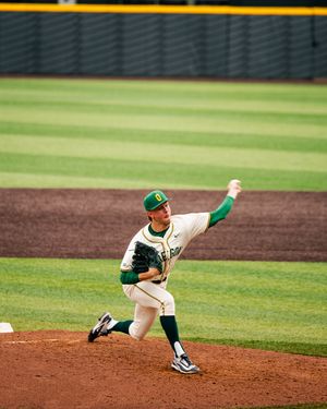 Oregon Ducks pitcher in white and green uniform delivers a pitch on the mound during a college baseball game.