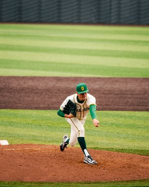 Oregon Ducks baseball pitcher in white and green uniform mid-windup on the mound during a college baseball game.
