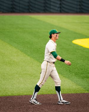 Baseball player in green and white uniform walking on field during a game.