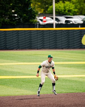 Oregon Ducks baseball infielder in ready position on the diamond during a college baseball game at a green outfield stadium.