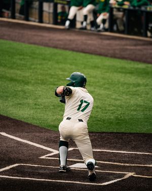 Baseball player #17 in green helmet and white uniform kneels at home plate during a college baseball game.