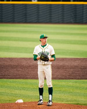 Oregon Ducks baseball pitcher standing on the mound in white and green uniform with glove ready.