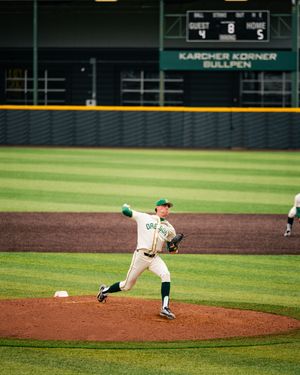 Oregon Ducks pitcher winds up to throw on the mound during a college baseball game at a green-trimmed stadium.
