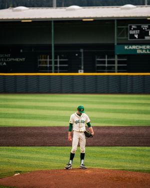 Baseball pitcher in green and white uniform stands on the mound at a professional stadium during a game.