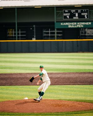 Baseball pitcher in green and white uniform mid-throw on a dirt mound at Karcher Korner Bullpen stadium.