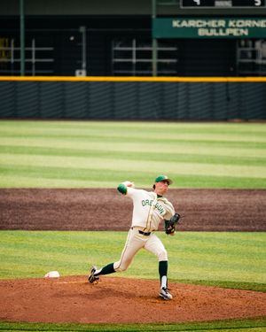 Oregon Ducks pitcher throwing a baseball on the mound at a college baseball stadium bullpen.
