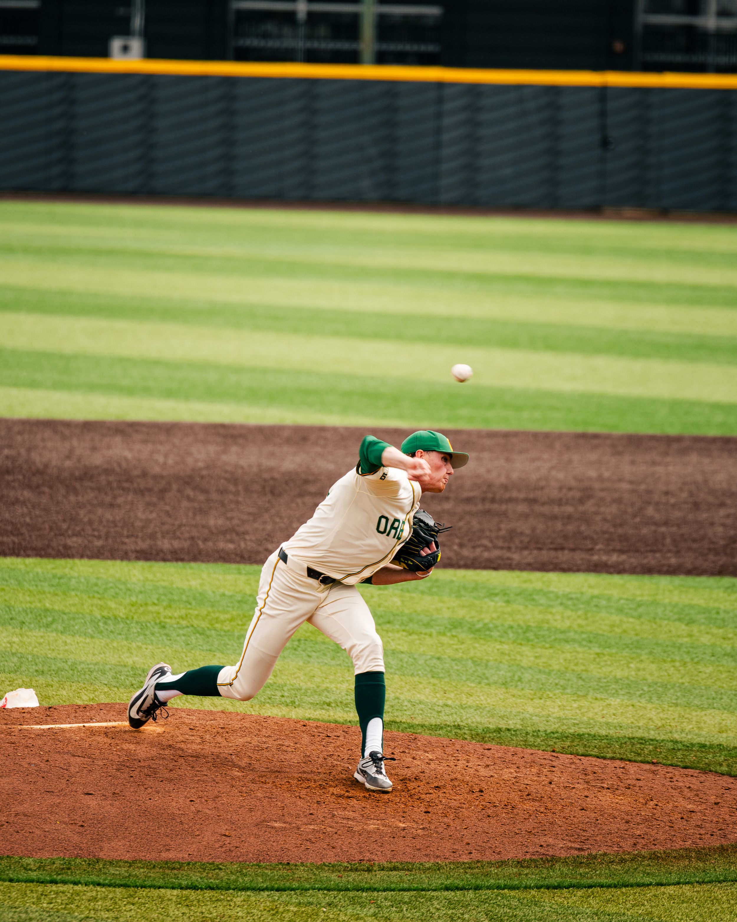 Oregon Ducks baseball pitcher in white uniform throwing a pitch from the mound during a college baseball game.