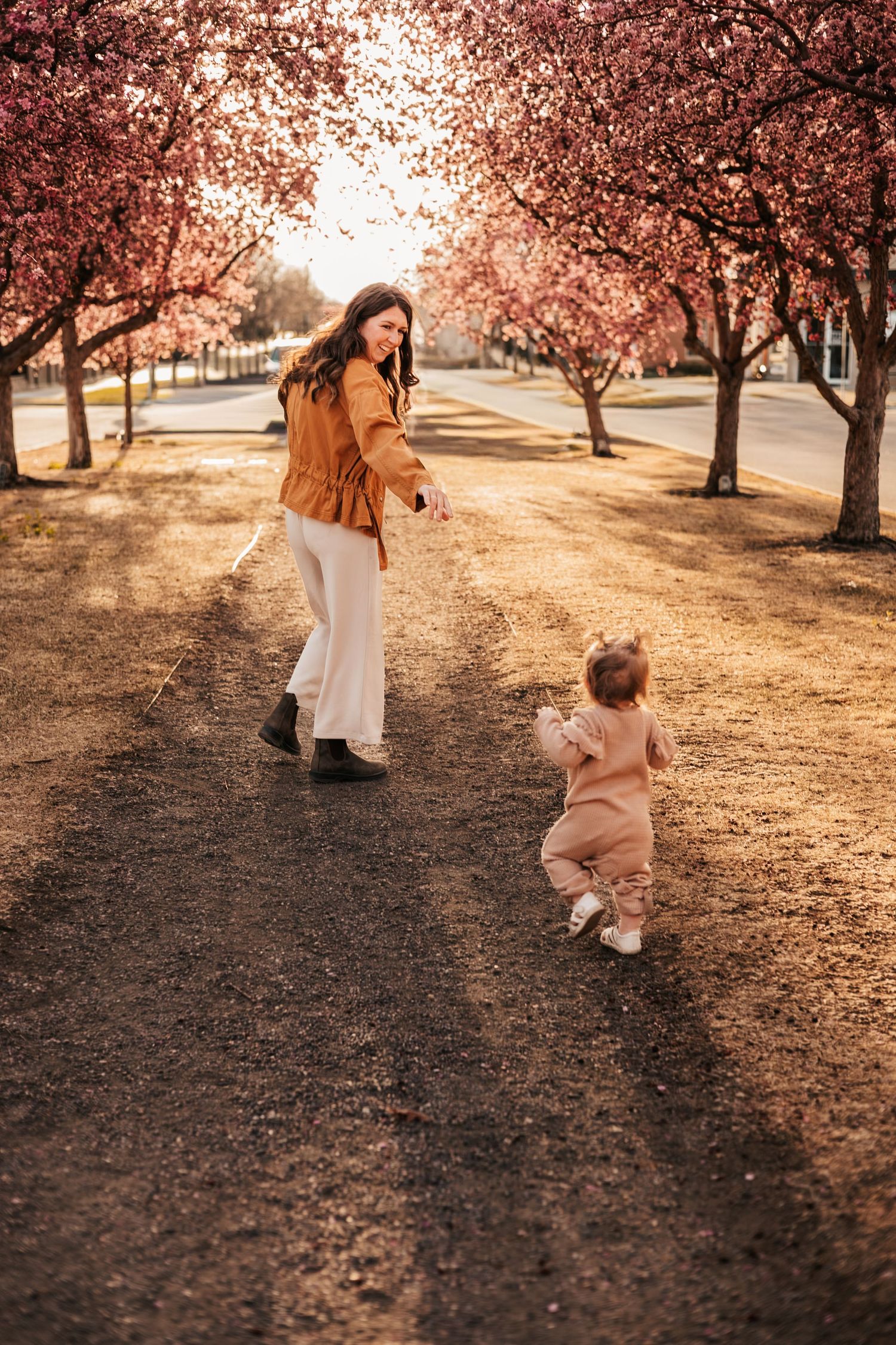 Mother and toddler walking together under blooming pink cherry blossom trees in spring  |How to Get Nice Family Photos with a toddler