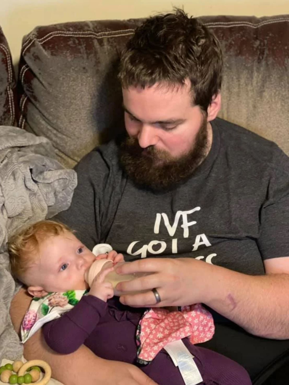 A tender moment as a baby receives a bottle while being held on a couch.