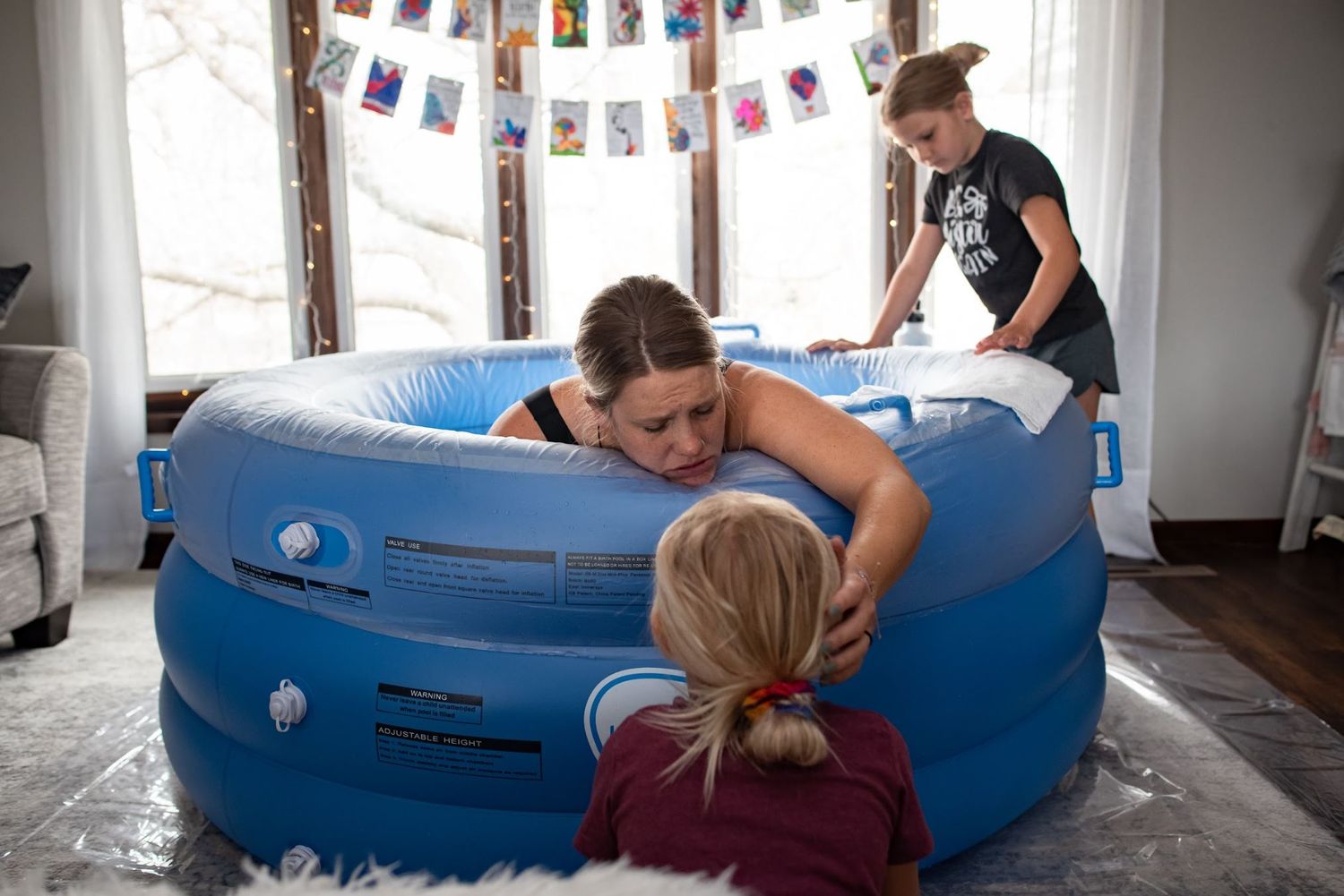 People gathered around blue inflatable birthing pool with decorative banners in background.