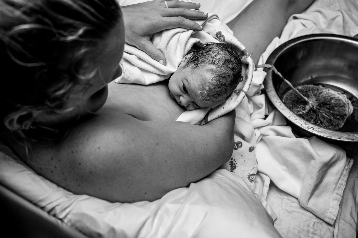A black and white image captures the first moments after birth as parent meets newborn.