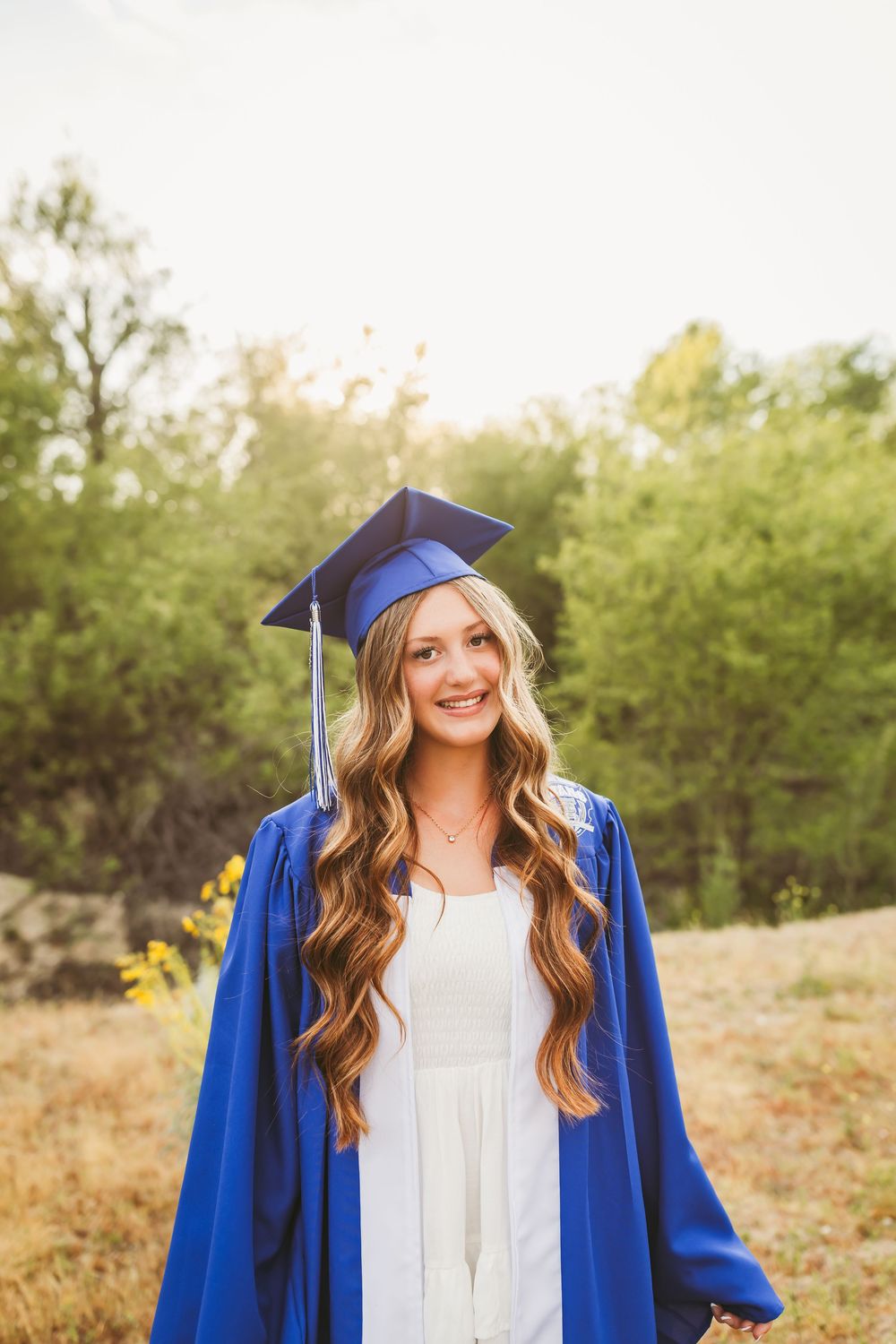 a senior girl in her blue cap and gown standing in a field with heidi grace photo