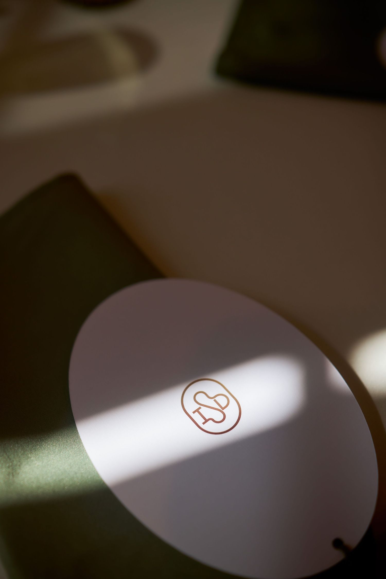 White oval card with a small red logo resting on a dark green surface in soft natural light.
