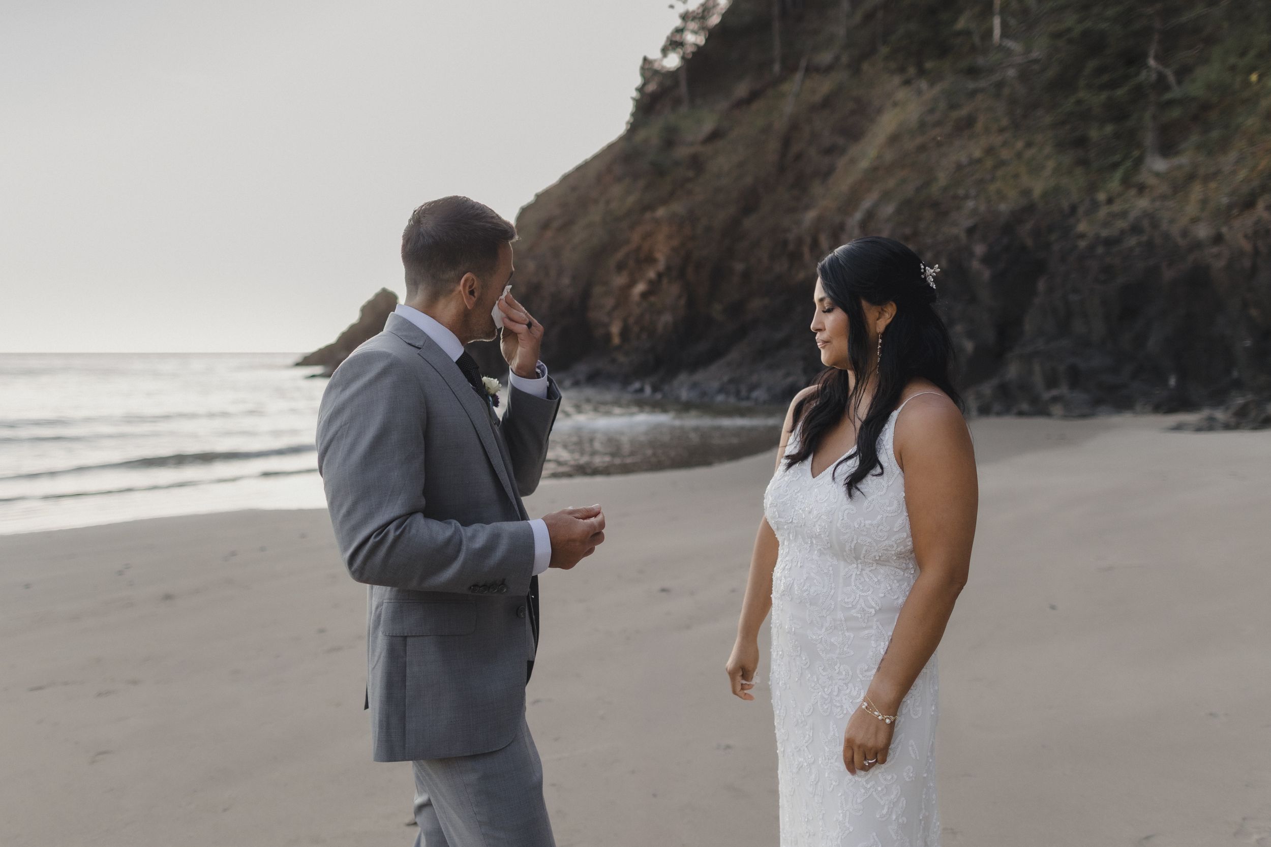 Couple exchanging vows on a sandy beach during an intimate elopement ceremony with coastal cliffs in the background.