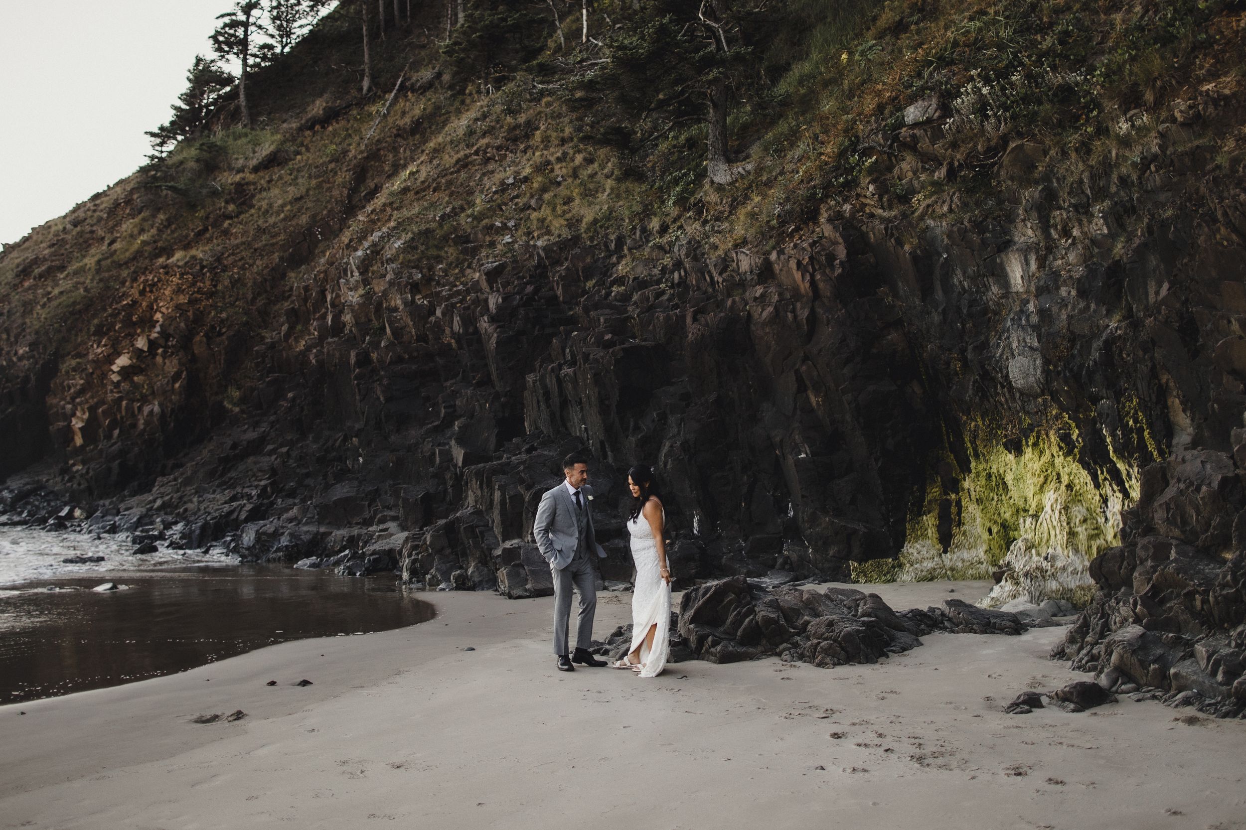A couple exchanges vows on a secluded sandy beach beside dramatic rocky cliffs.