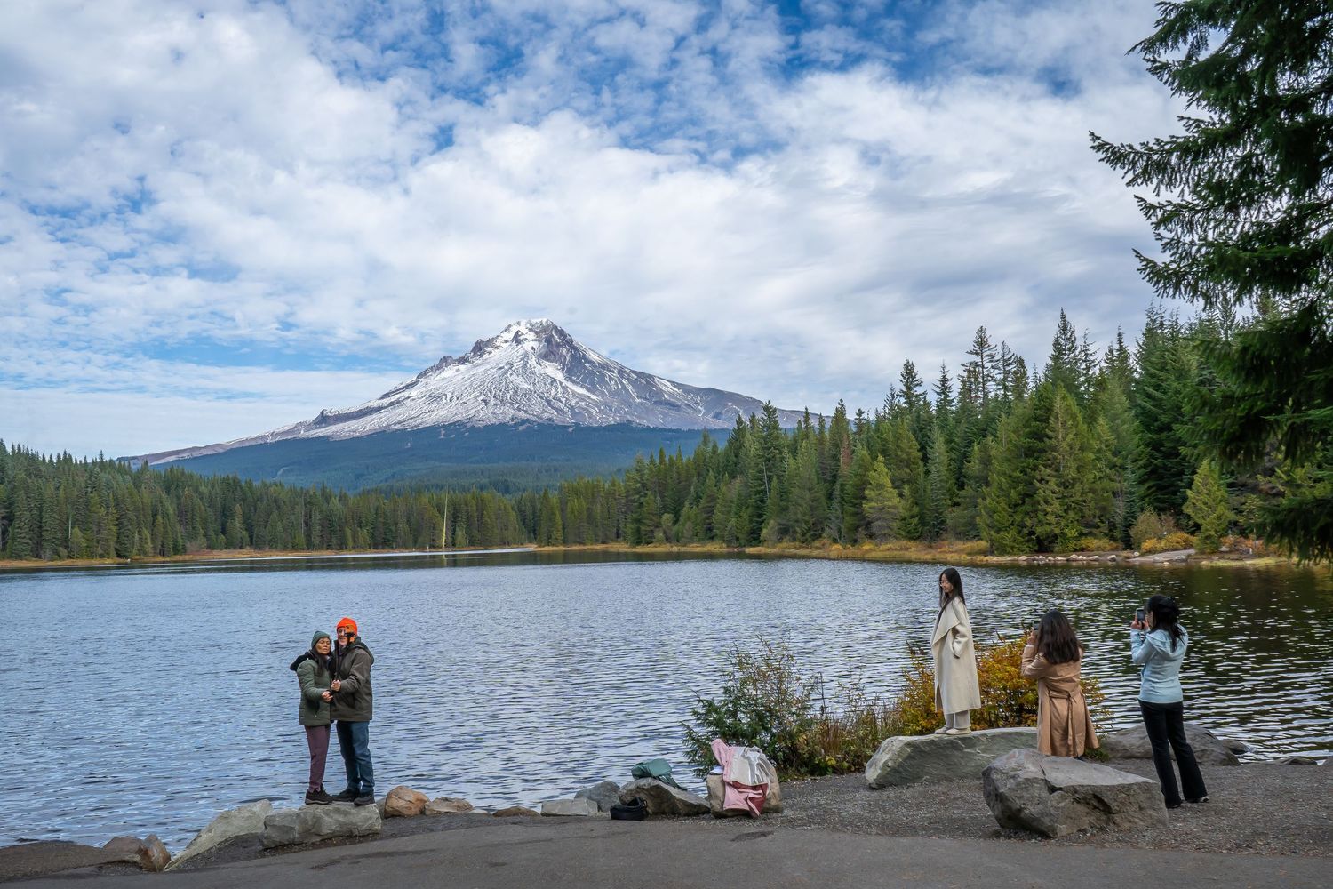 A scenic mountain lake surrounded by evergreen forest and snow-capped peaks under cloudy skies.