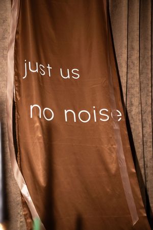Brown satin curtain with white text reading just us no noise at an intimate wedding venue.